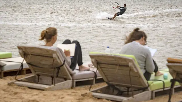 Deux vacanciers européens s'allongent sur des chaises longues au Sahara occidental, tandis qu'un autre fait du kitesurf dans la mer